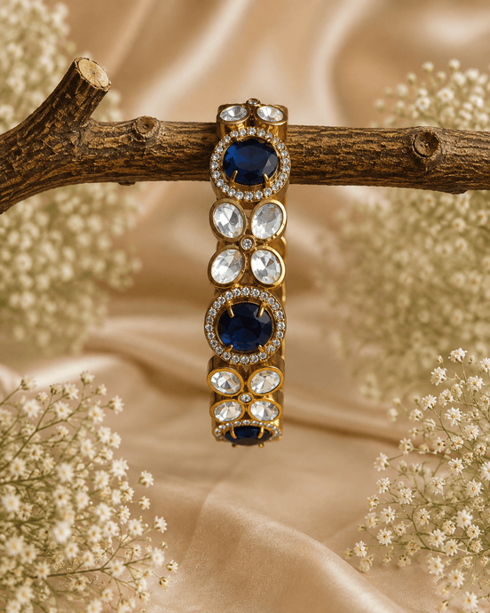 Gold-tone stone bracelet with dark blue oval stones and clear round accents, on branch