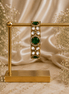 Gold-tone stone bracelet with green oval centers and clear round accents, on stand