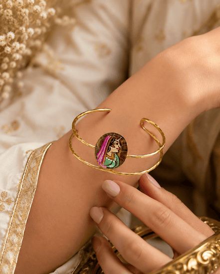 Gold-tone open cuff bracelet with oval enamel face on wrist, close-up