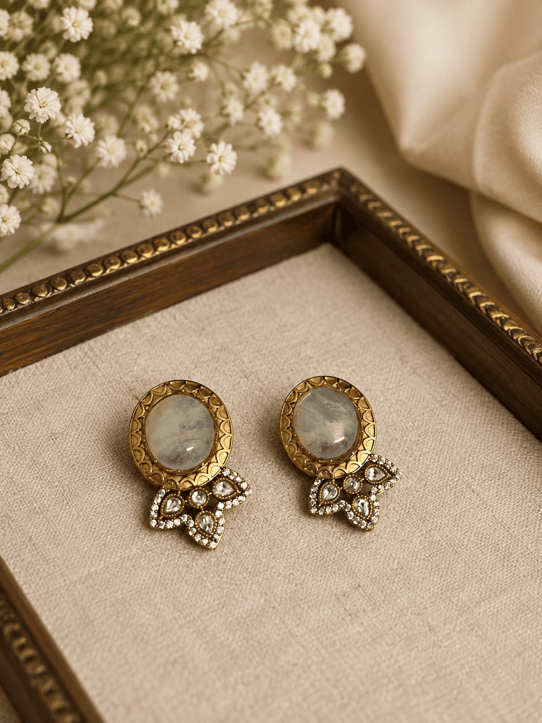 Light gray oval stud earrings with ornate gold bezel and crystal bow dangles