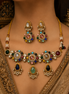 Jeweled gold-toned necklace set with matching drop earrings on neckline; multicolor stones.