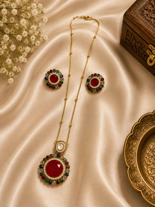 Gold pendant set with circular red center medallion and green blue gemstone accents