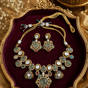 Jewelry set on maroon cushion: gold-tone choker necklace with green gemstone drops