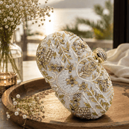 White beaded clutch with gold-toned floral and star motifs; rounded top and clasp.