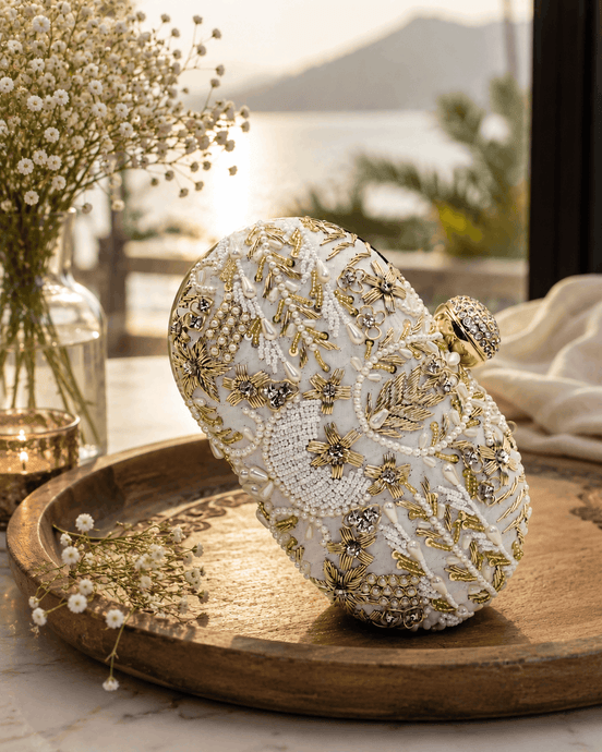 White beaded clutch with gold-toned floral and star motifs; rounded top and clasp.