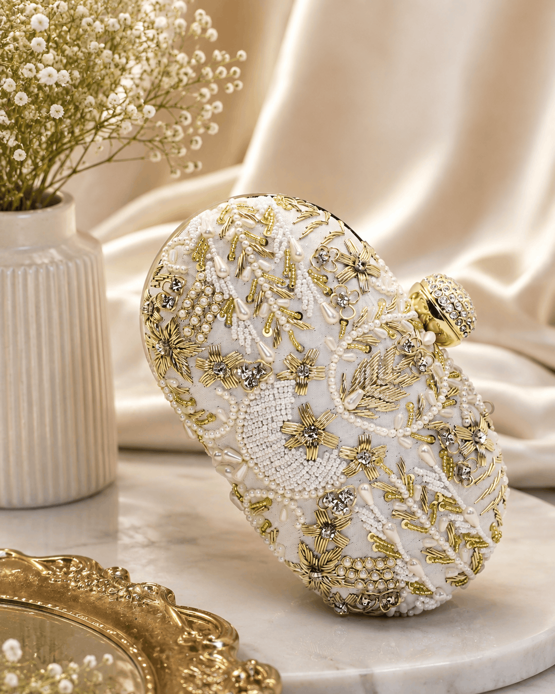 White beaded clutch close-up with gold-toned embellishments; rounded top with gold clasp.