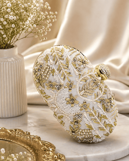 White beaded clutch close-up with gold-toned embellishments; rounded top with gold clasp.